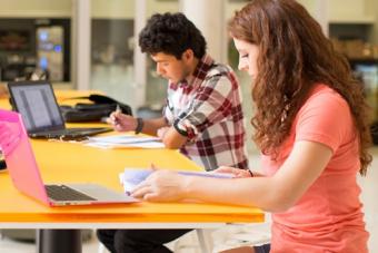 Two college students studying at a table with laptops